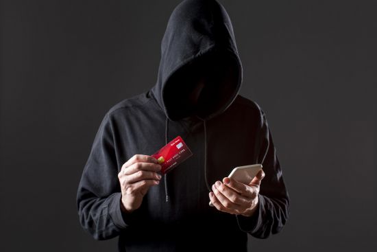front view of male hacker holding smartphone and credit card